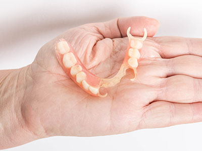 An elderly hand holding a prosthetic denture with visible teeth and gums.