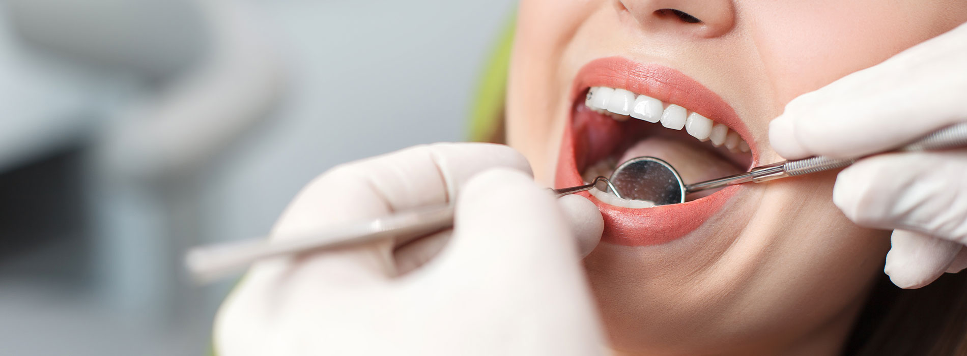 The image shows a person undergoing dental care, with their mouth open wide, revealing teeth being worked on by a dentist s hands visible behind a transparent barrier.