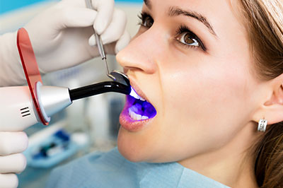 The image features a person receiving dental treatment, with a dentist s hand visible holding a dental instrument near the patient s mouth, which appears to be purple in color.