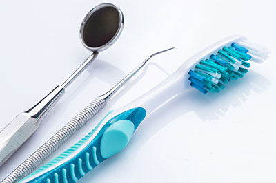 The image displays dental instruments including a toothbrush with blue bristles on a white surface, with a focus on oral hygiene tools.