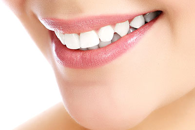 The image shows a close-up of a person s smiling face with a focus on their teeth and lip area, set against a blurred background.