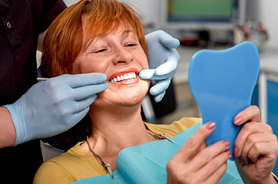 A woman sits in a dental chair with a blue mouthguard placed on her teeth, smiling at the camera while holding up a toothbrush.