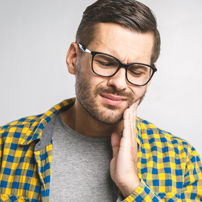 The image shows a man with glasses, wearing a plaid shirt, with his hand on his chin, seemingly in deep thought or contemplation.