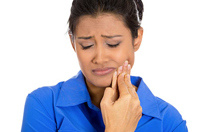 A woman with her eyes closed, holding her face with both hands, appears distressed while looking upwards.