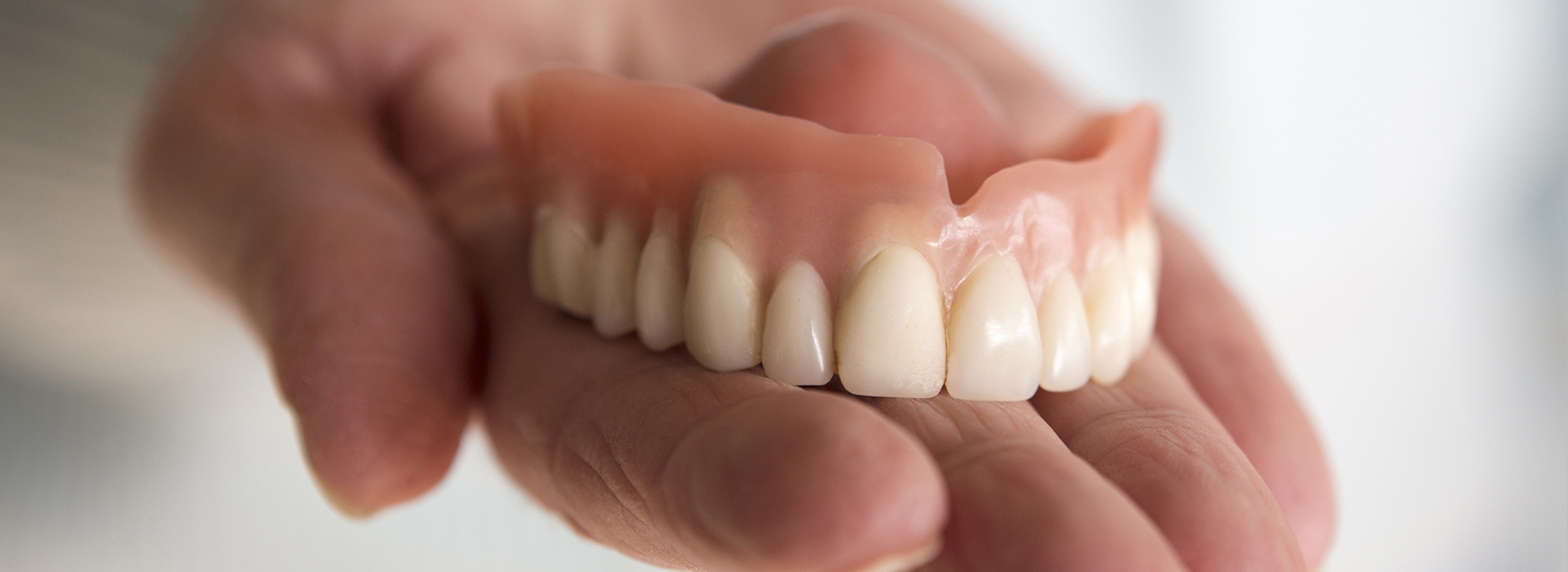 An elderly person holding a set of dentures with their teeth showing.