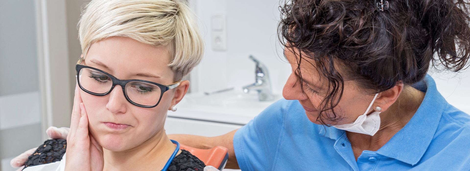 A woman with glasses is receiving dental care from a dentist in an office setting.