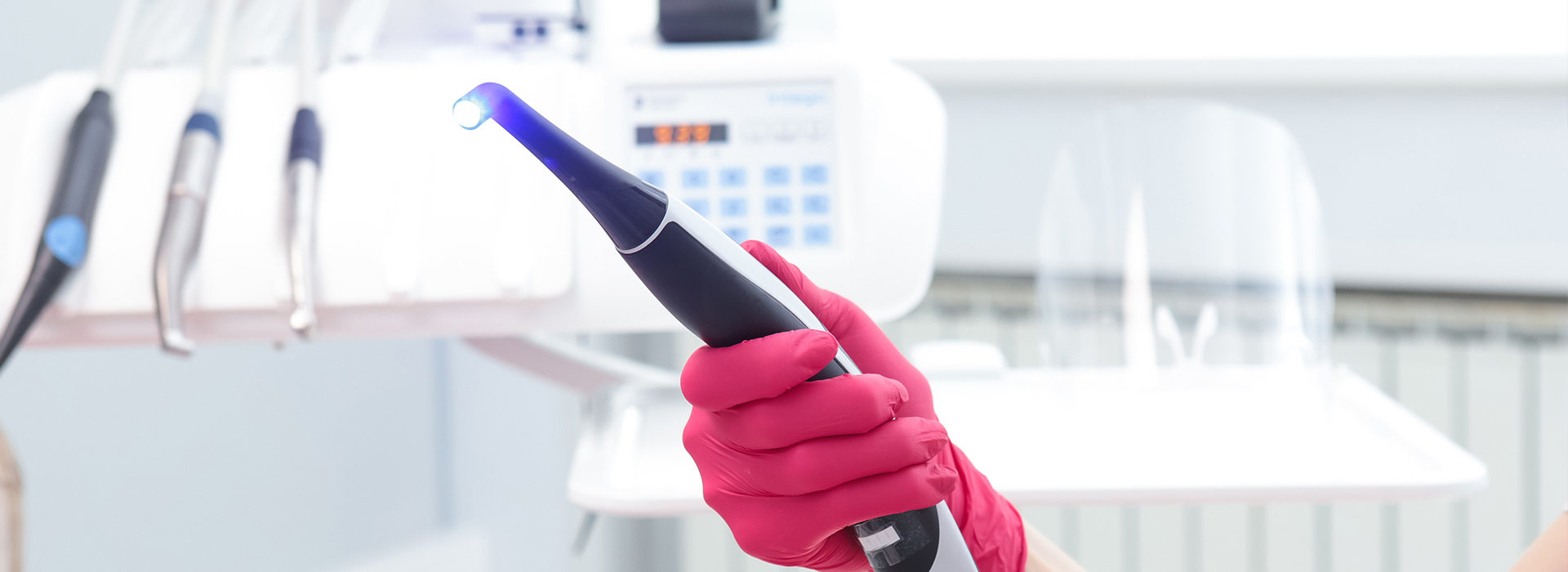 The image shows a person wearing pink gloves holding a blue device with a screen, likely an electronic tool or gadget being used in a laboratory setting.