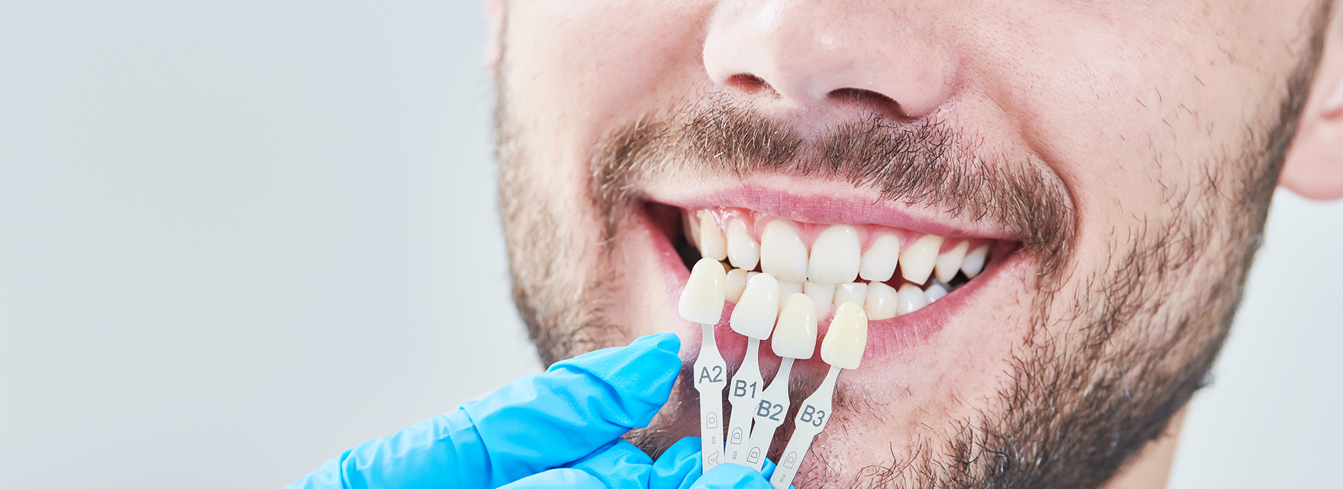 The image shows a person wearing a white lab coat and holding dental tools, with a focus on their smiling face and teeth.