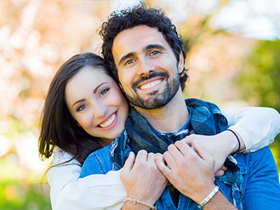A man and woman are hugging each other, smiling at the camera.