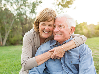 An older couple embracing each other outdoors during daylight hours.