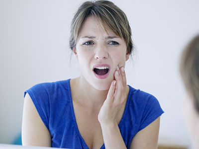 The image shows a woman with her mouth open wide, displaying a toothpaste advertisement on her teeth, with a concerned expression while looking at a reflection in a mirror.