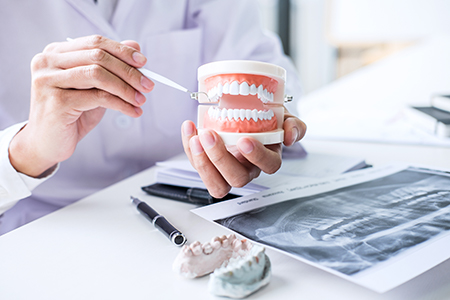 The image shows two photos of a dental professional holding a tooth model with a magnifying glass over it, demonstrating the use of a dental tool on a tooth impression.