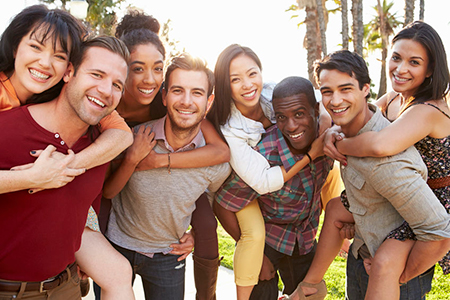 The image shows a group of young adults posing together for a photo with smiles on their faces they are standing outdoors, possibly at a social event, during daylight hours.