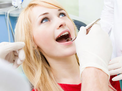 A woman undergoing dental treatment with a dentist performing the procedure, set against a blurred background of a dental office.