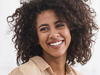 A woman with curly hair smiles at the camera, wearing a beige top.