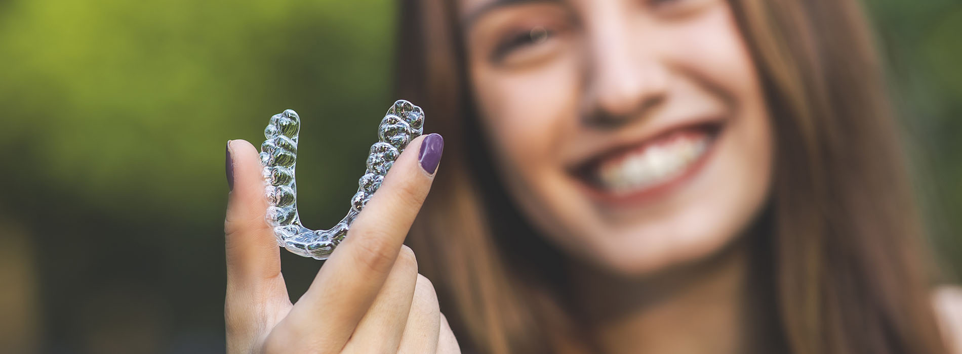 The image shows a person holding a small, clear plastic object with a heart shape on it, smiling at the camera.